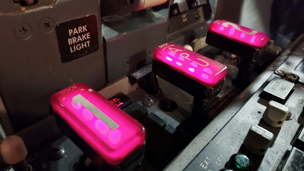 Close-up of the Boeing 737 NG fire suppression panel showing illuminated discharge handles for engine and APU fire bottles, with labeled switches and park brake indicator nearby.